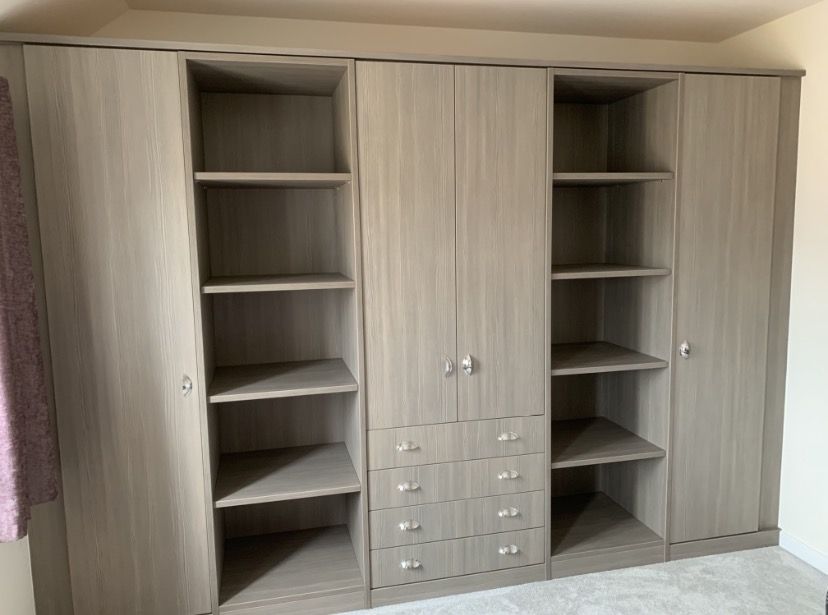 Fitted bedroom wardrobes with open shelving, drawers and a grey oak finish