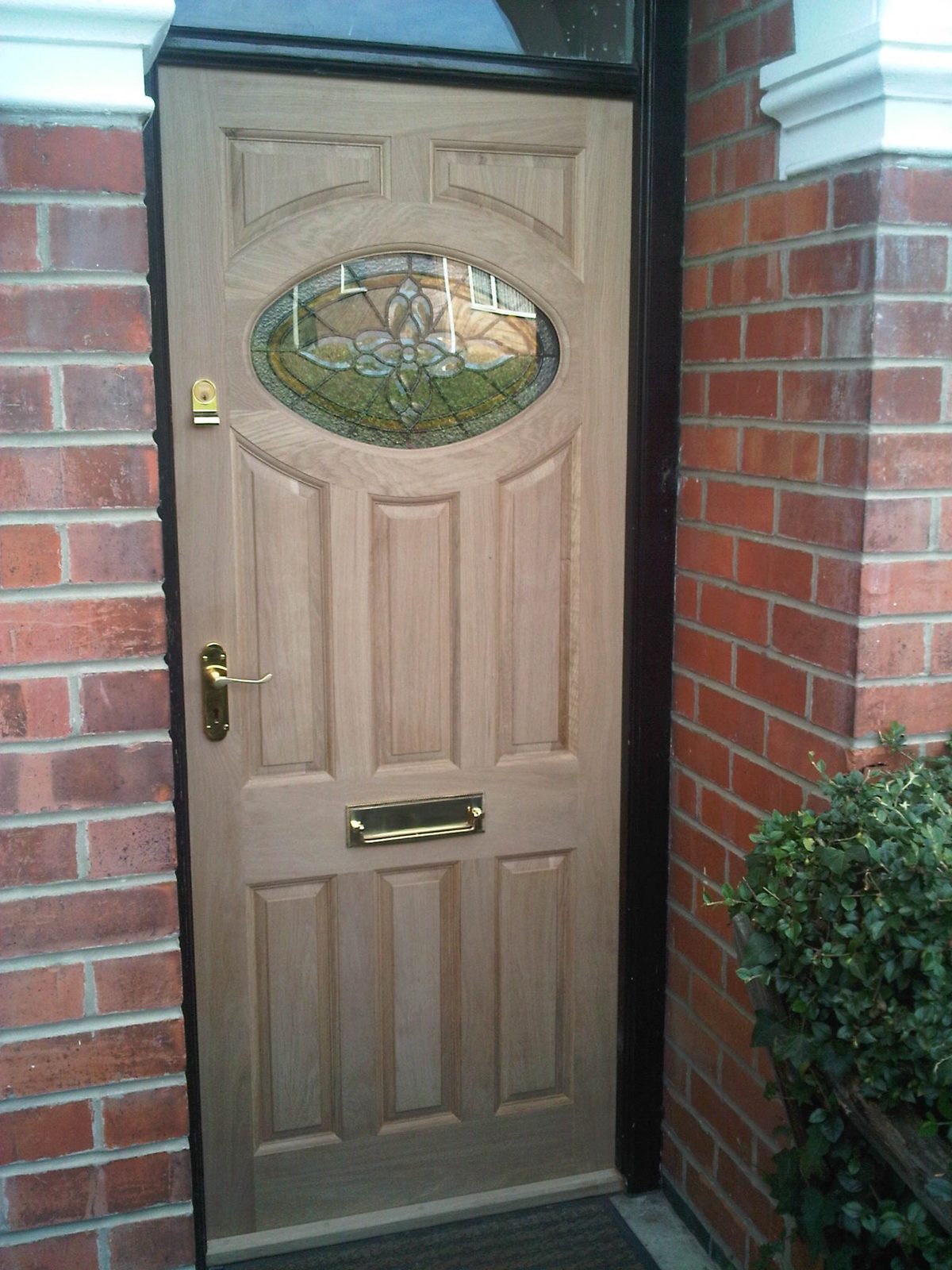 Solid oak front door with oval stained-glass panel and brass furniture